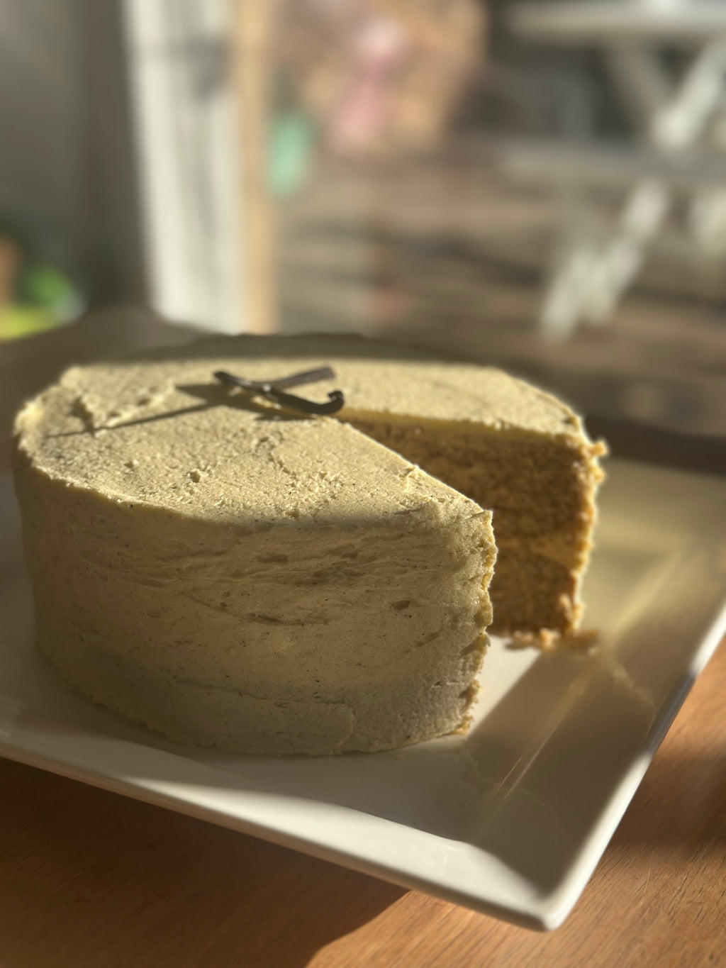 A freshly baked, 2 layer, gluten-free vanilla bean cake made with unspent vanilla bean powder and no added sugar, sliced open and presented on a white plate.