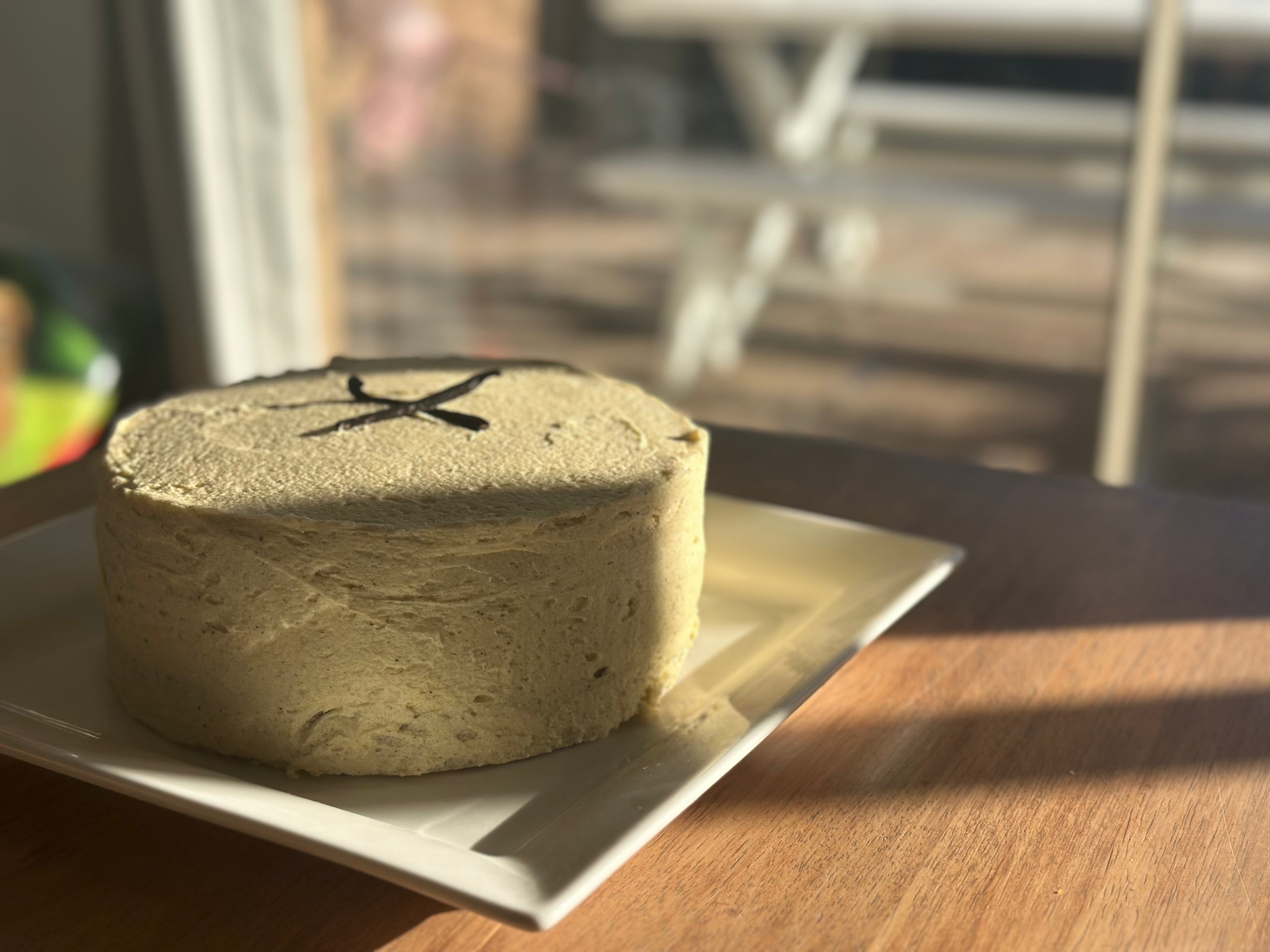 A freshly baked, 2 layer, gluten-free vanilla bean cake made with unspent vanilla bean powder and no added sugar, presented on a white plate.
