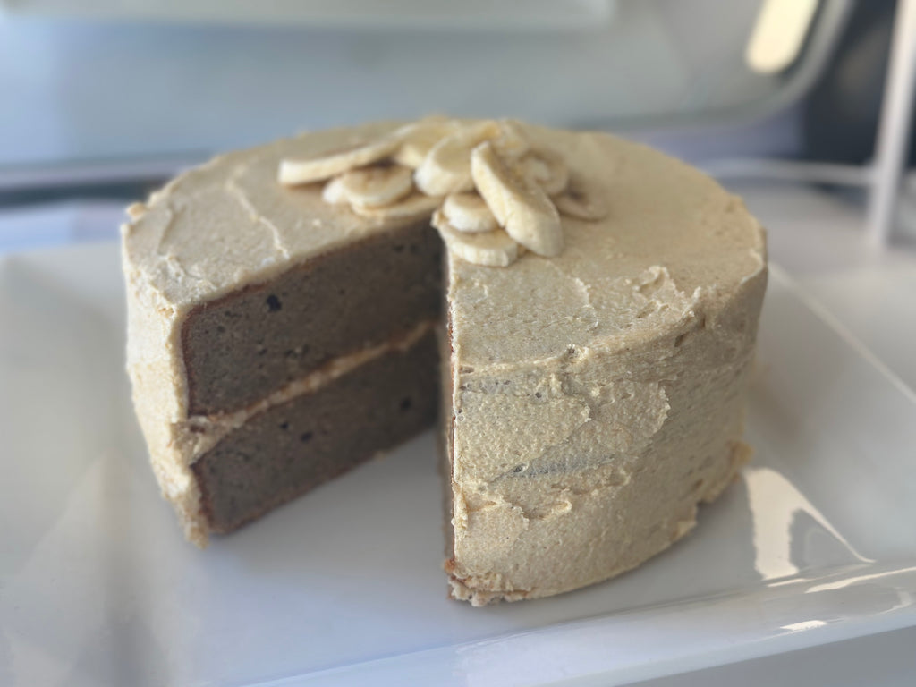 A freshly baked, premium gluten-free banana cake featuring a natural yellow hue from organic fruit powder, cut open and presented on a white plate.