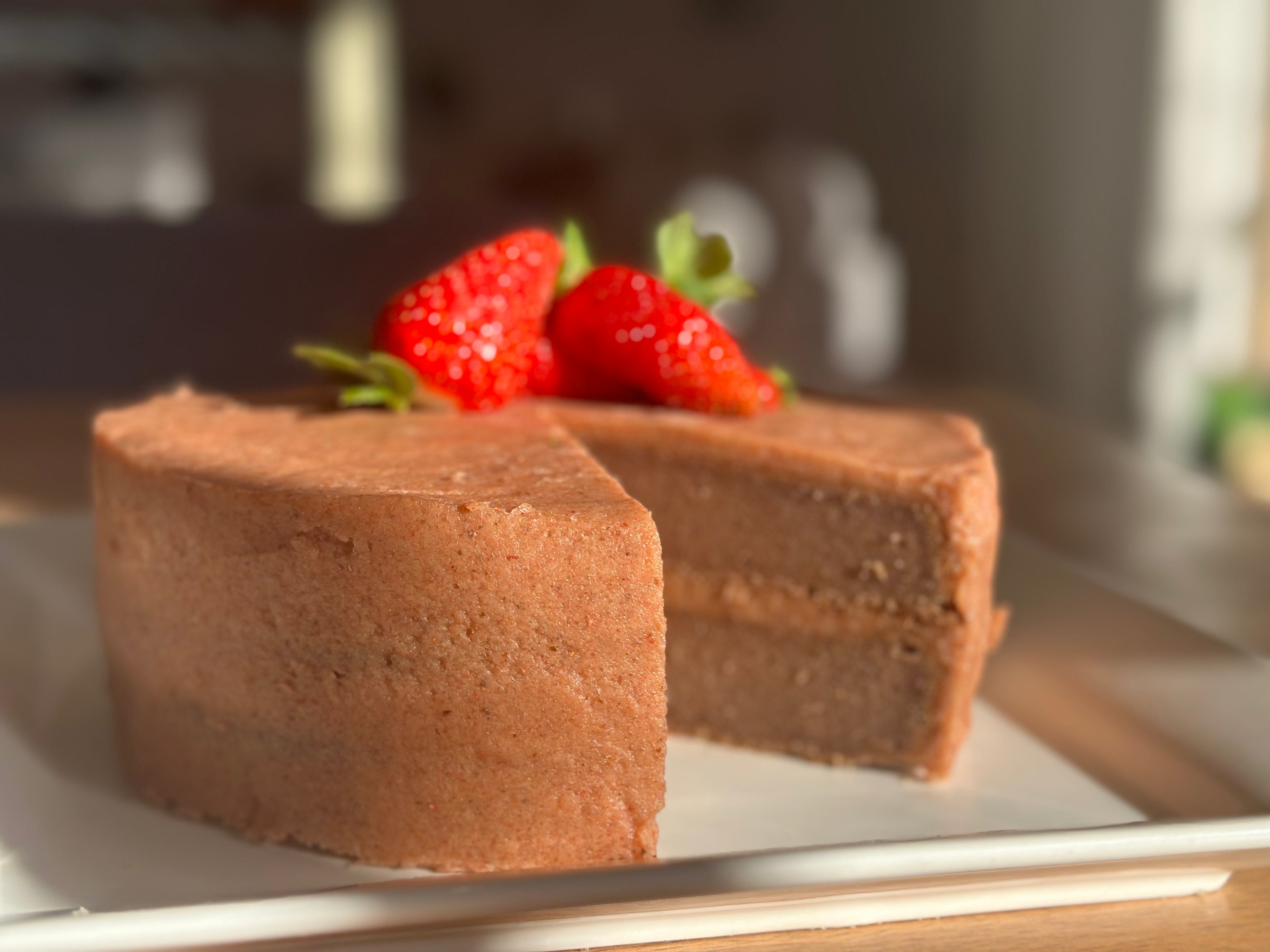 A freshly baked, premium gluten-free strawberry cake featuring a natural pink hue from organic fruit powder, cut open and presented on a white plate.