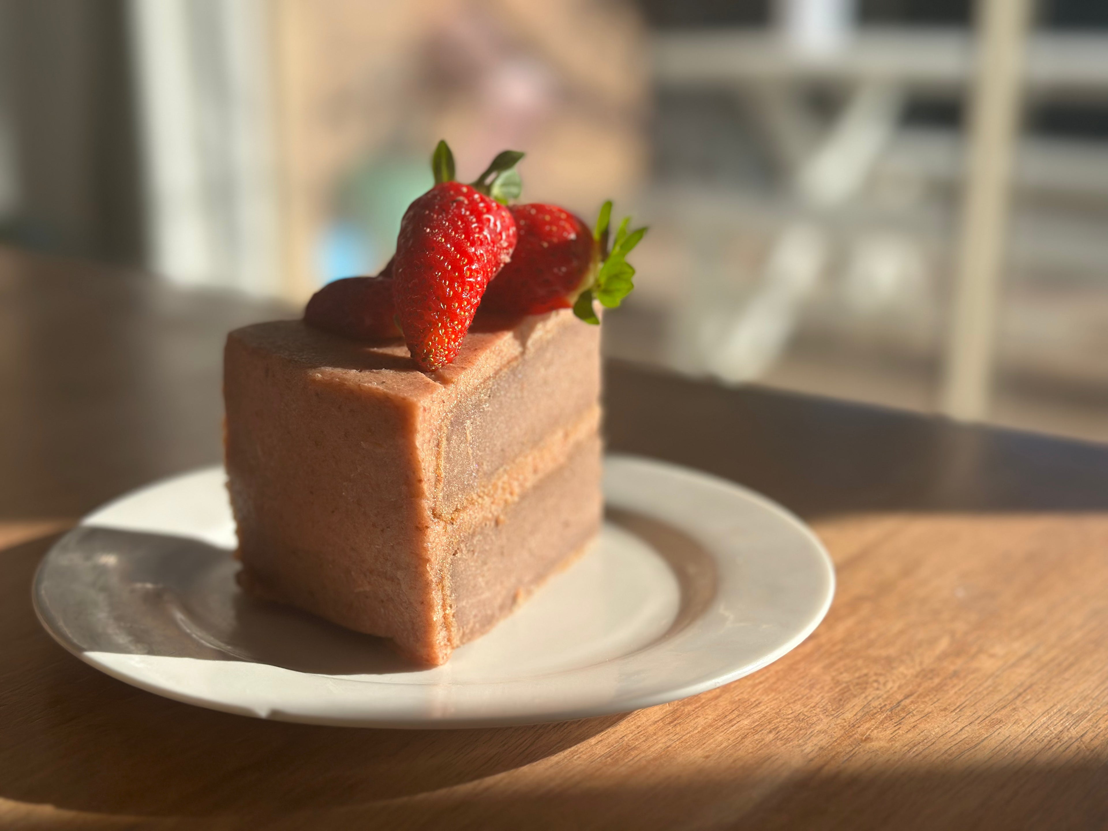 A freshly baked slice of, premium gluten-free strawberry cake featuring a natural pink hue from organic fruit powder, presented on a white plate.