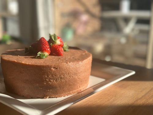 A freshly baked, premium gluten-free strawberry cake featuring a natural pink hue from organic fruit powder, presented on a white plate.