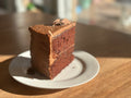 A freshly baked, slice of rich gluten-free chocolate cake made with organic cacao and no added sugar, presented on a white plate.