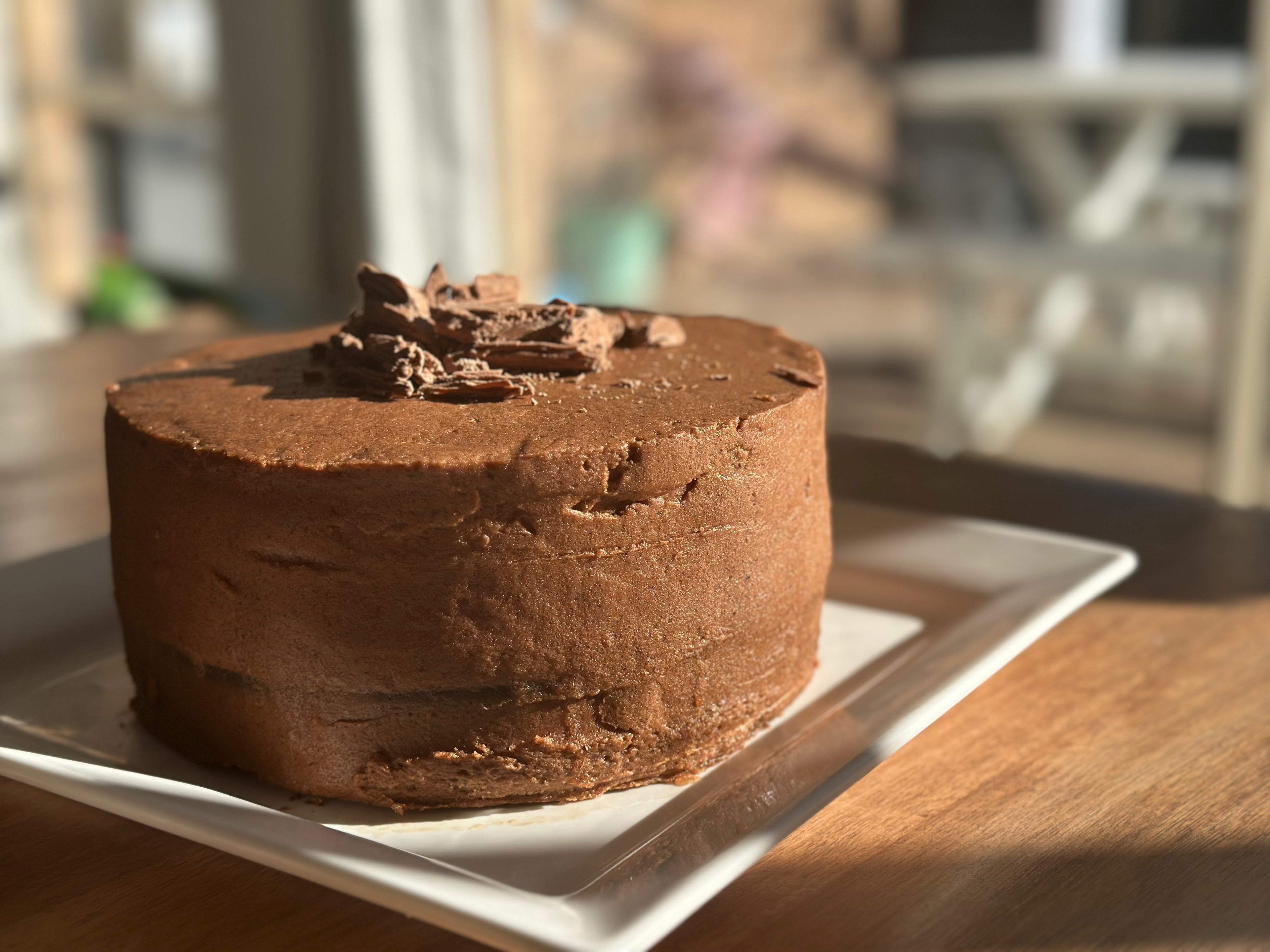 A freshly baked, 2 layer, rich gluten-free chocolate cake made with organic cacao and no added sugar, presented on a white plate.