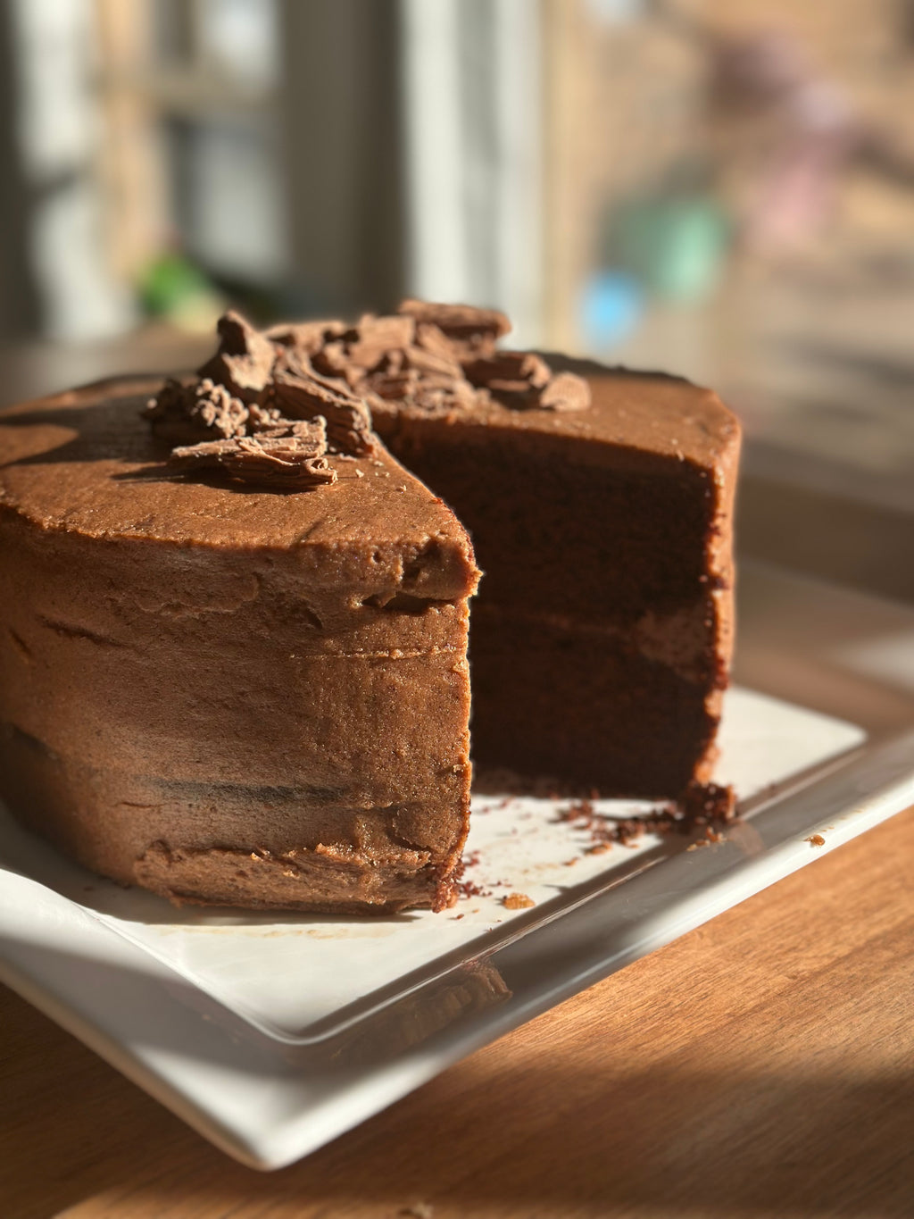 A freshly baked, 2 layer, rich gluten-free chocolate cake made with organic cacao and no added sugar, sliced open and presented on a white plate.
